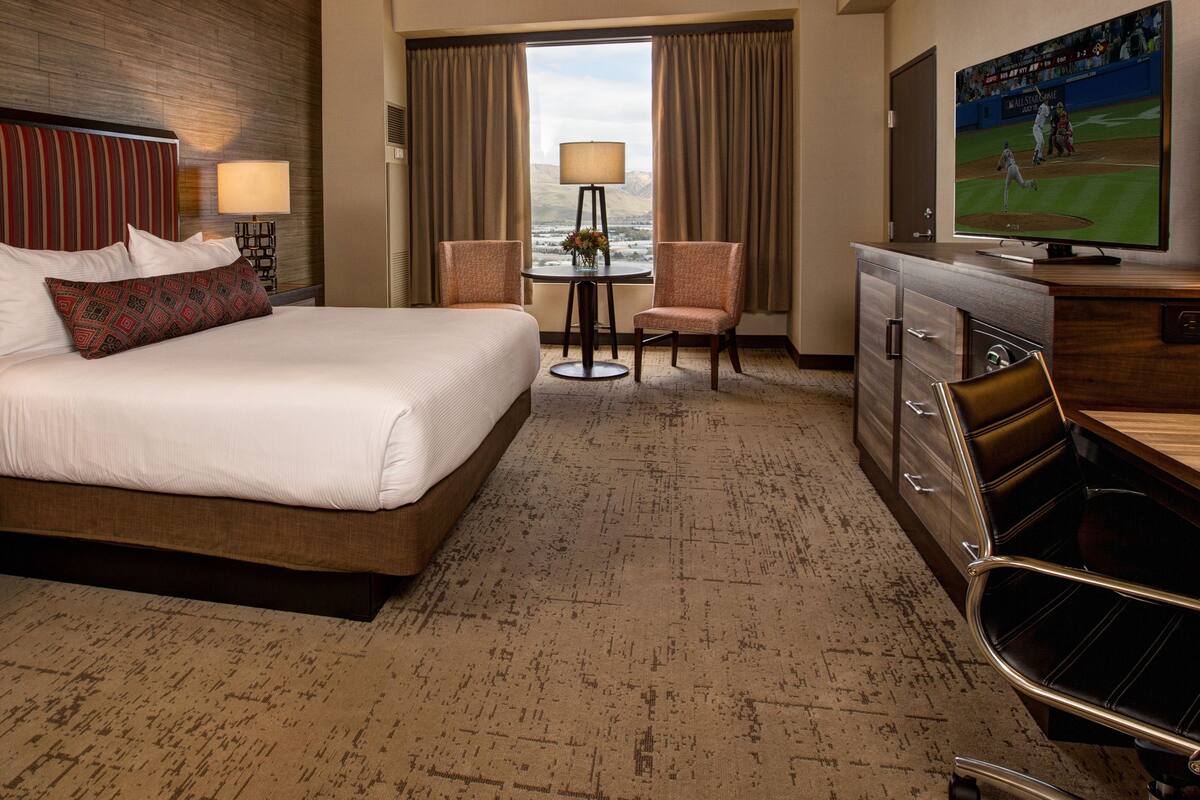 A hotel room with a large bed, a desk with a TV, a chair, and a view of the outdoors.