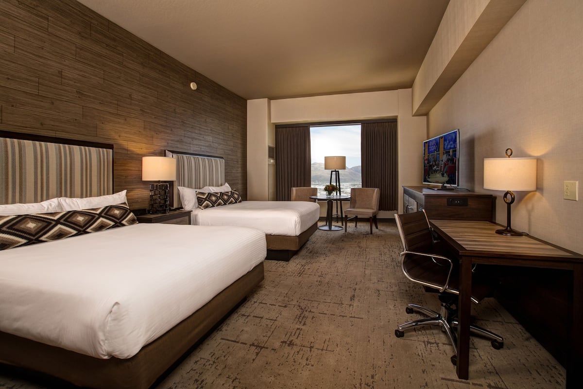 A hotel room with two beds, a desk, a chair, a TV, and a view of the mountains.