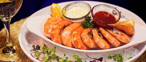 A plate of cooked shrimp with lemon wedges and two small bowls of dipping sauces, served on a bed of ice.
