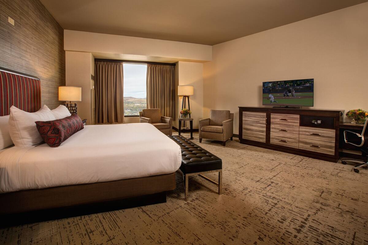 A hotel room with a large bed, a desk, two chairs, a TV, and a view of the outdoors.