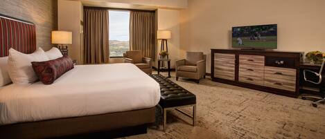A hotel room with a large bed, a desk, two chairs, a TV, and a view of the outdoors.