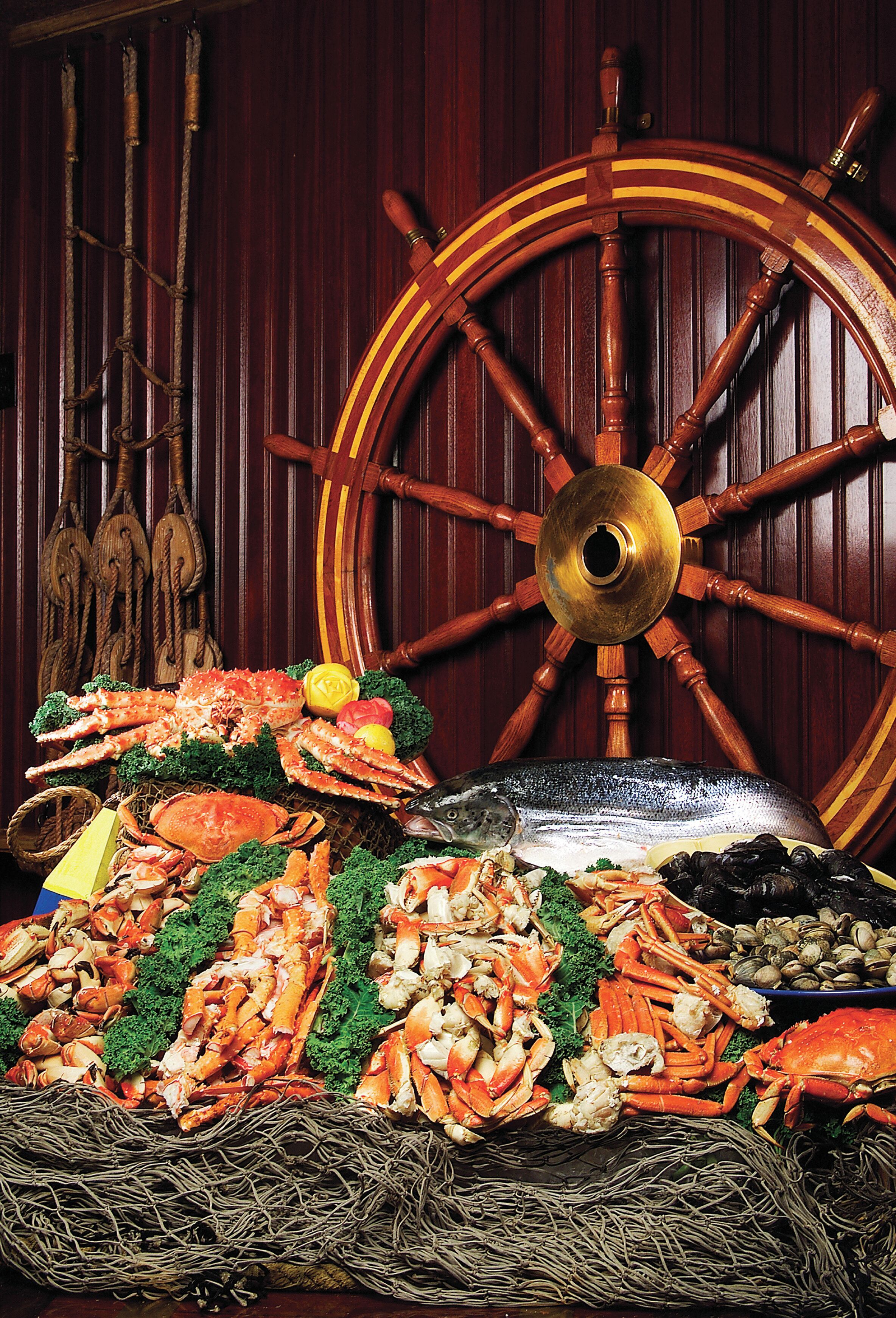 A seafood display with various types of seafood, including crabs and fish, arranged on a table with a large wooden wheel in the background.