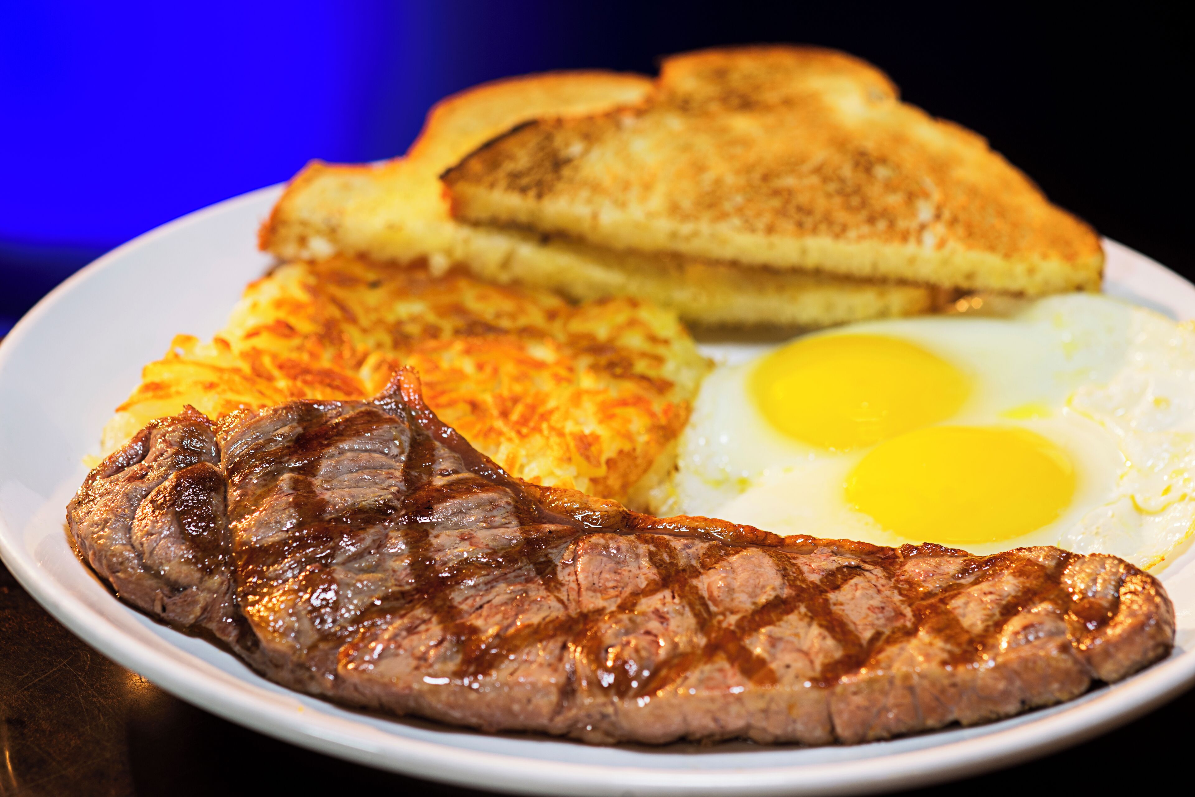 A plate with a steak, two fried eggs, hash browns, and toast.