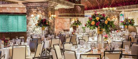 A banquet hall with round tables, chairs, and floral centerpieces.