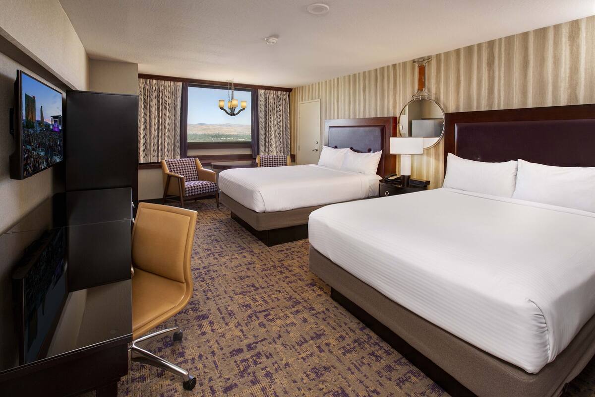 A hotel room with two beds, a TV, a desk, a chair, and a view of the desert.