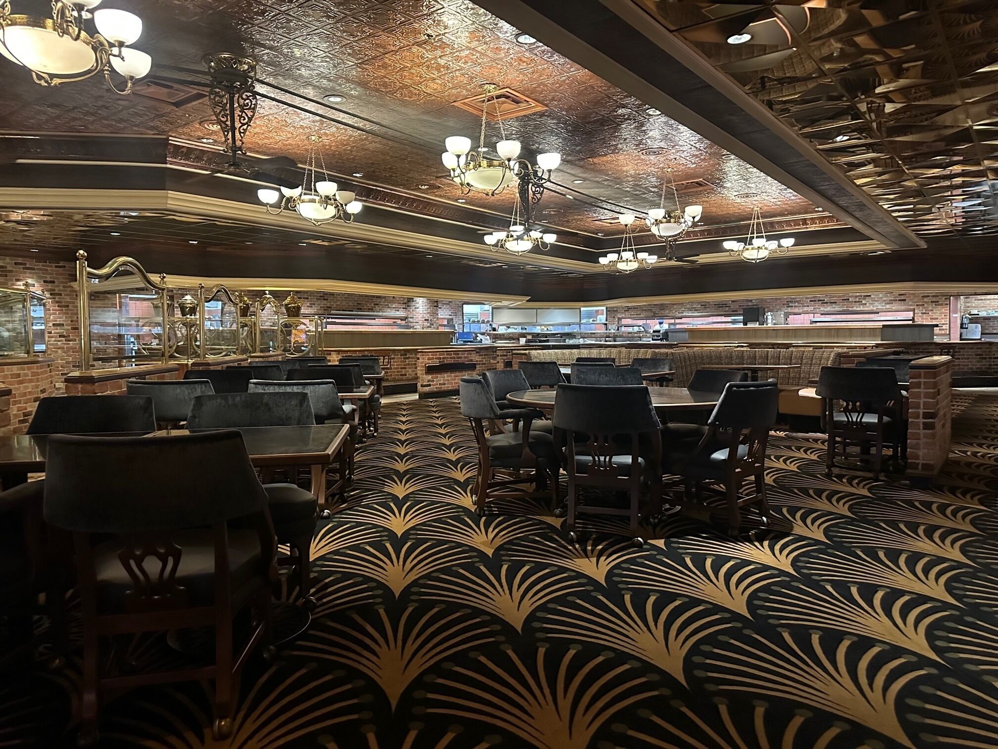 L’intérieur d’un restaurant présente un tapis à motifs, des murs en briques et plusieurs espaces de restauration, notamment des banquettes et des tables.