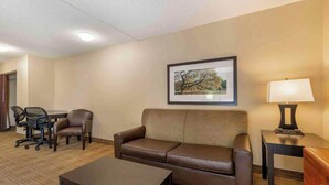 Une chambre d’hôtel avec un canapé en cuir marron, une petite table, un bureau, une chaise et un tableau encadré au mur.