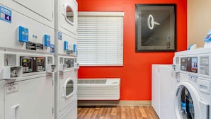 A laundry room with multiple washing machines and dryers, a vent, and a window with blinds. - Studio 6 Extended Stay Florence, KY - Meijer Dr./Cincinnati (Florence)