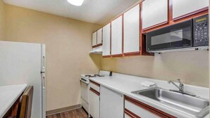 Une cuisine de taille réduite avec des meubles blancs, un four à micro-ondes, un évier et une cuisinière.