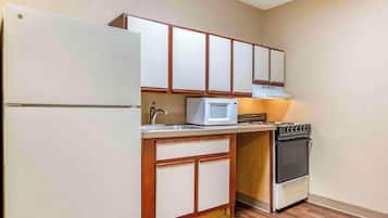 Una cuina compacta amb nevera, microones, fogó i armaris de fusta.