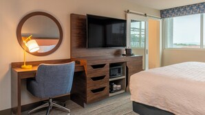 Een hotelkamer met een houten bureau, een stoel, een flatscreen-televisie, een bed met een witte dekbedovertrek en een groot raam met uitzicht op de stad.