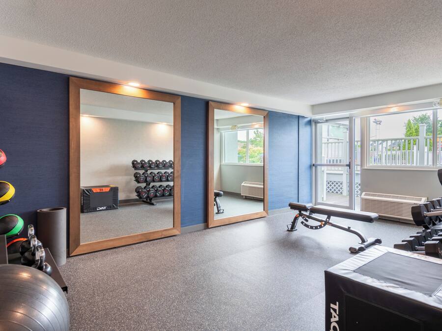 Une salle de sport équipée de matériel d’exercice, de miroirs et offrant une vue sur l’extérieur.