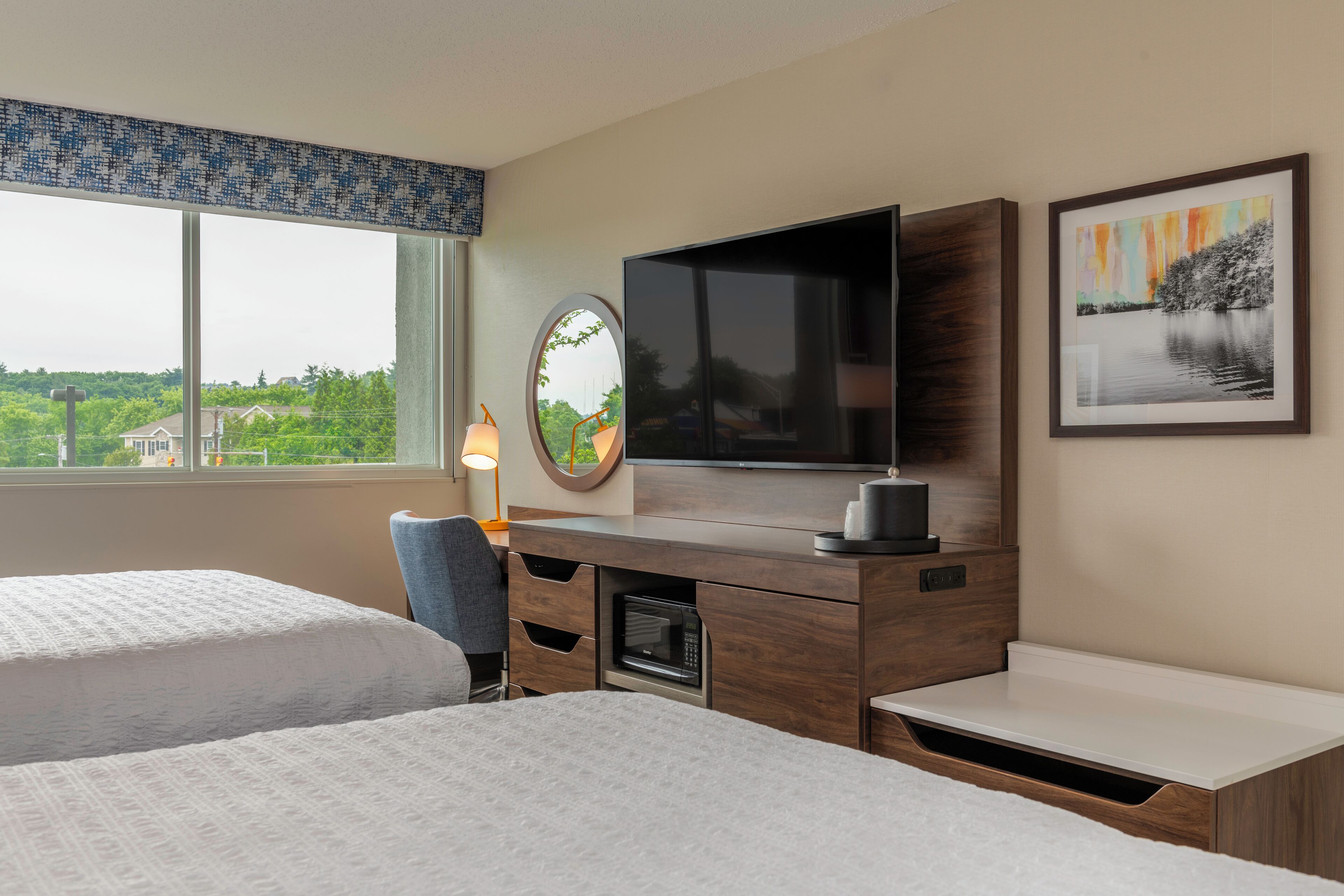 Habitación de hotel con dos camas, un escritorio, televisor de pantalla plana, microondas y ventana con vistas a zonas verdes.