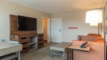 A hotel room with a TV, a desk, a chair, a sofa, and a lamp.