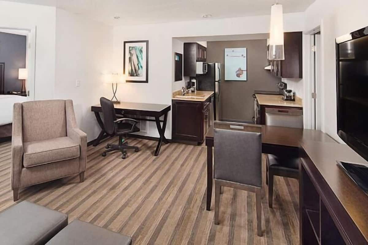 A hotel room with a bed, a desk, a chair, a TV, and a kitchenette.