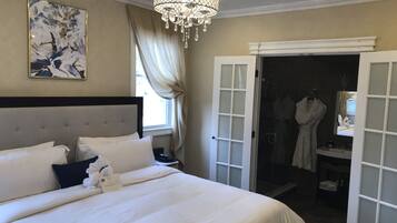 Habitación de hotel con una cama grande, una araña de cristal, un cuadro y un baño visible a través de una puerta abierta.