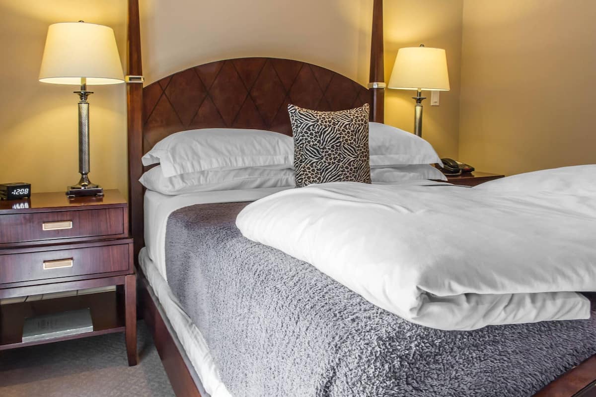 A neatly made bed with white linens and a grey blanket, flanked by two bedside lamps and a nightstand with a clock.