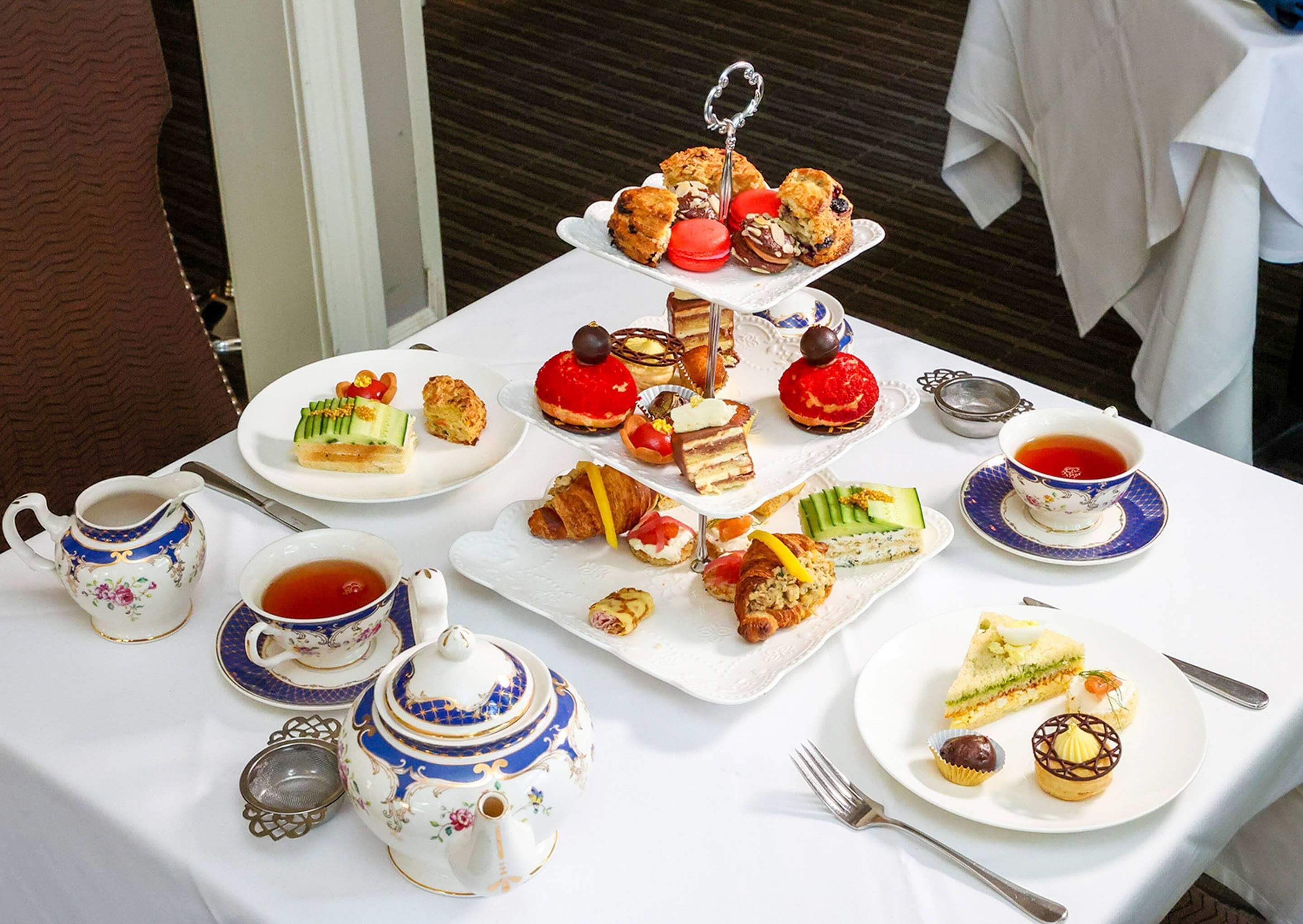 A table set with a variety of pastries, sandwiches, and tea cups, suggesting a tea service or buffet.