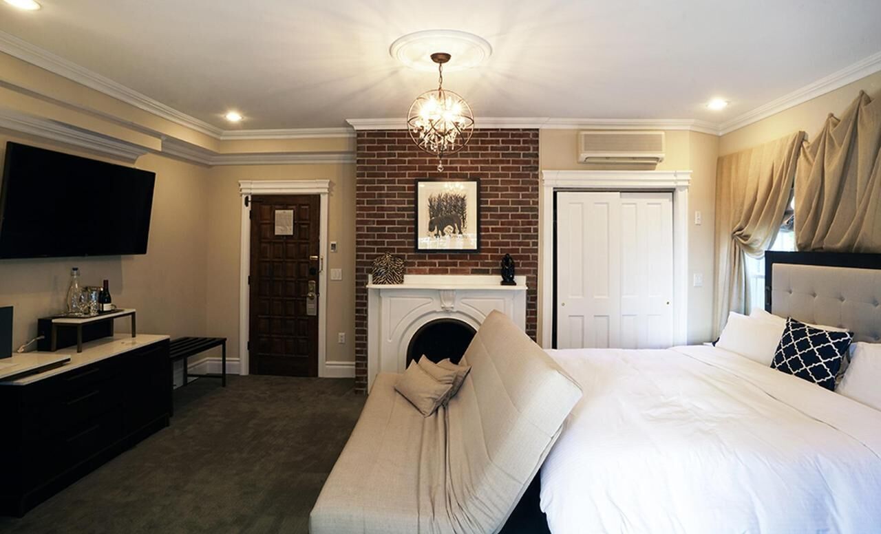 A hotel room with a bed, a television, a fireplace, and a chandelier.