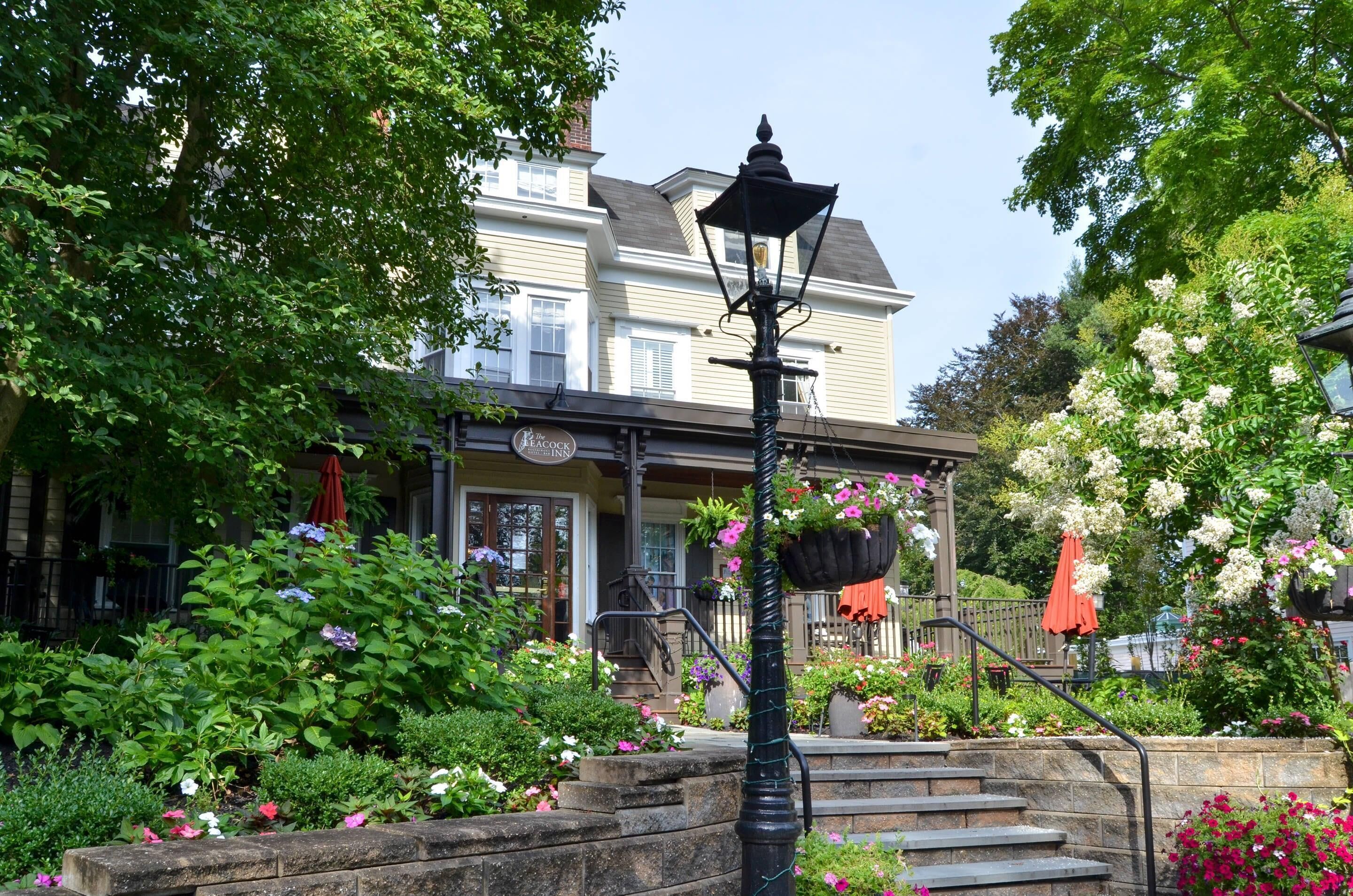 Une auberge traditionnelle avec un escalier en pierre menant à l’entrée, entourée d’une végétation luxuriante et de plantes en fleurs.