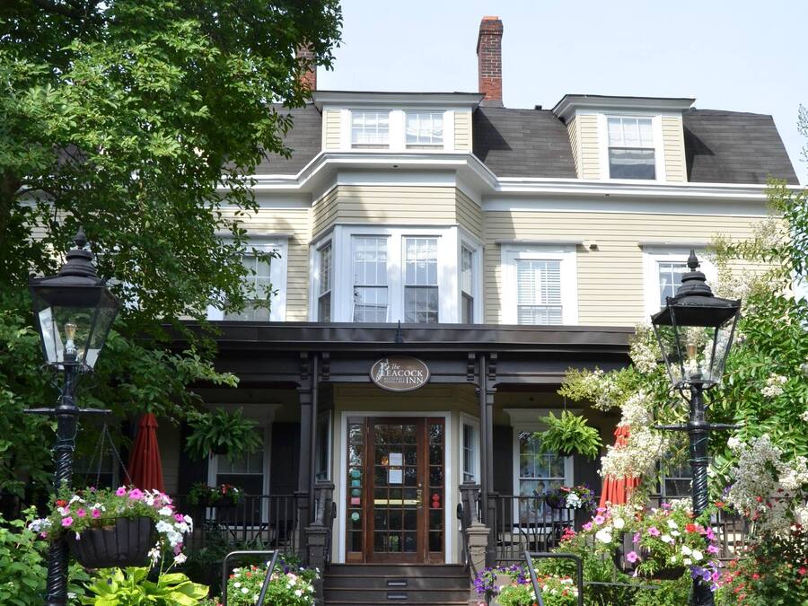 A two-story building with a porch, a sign reading "The Peacock Inn," and flower baskets.