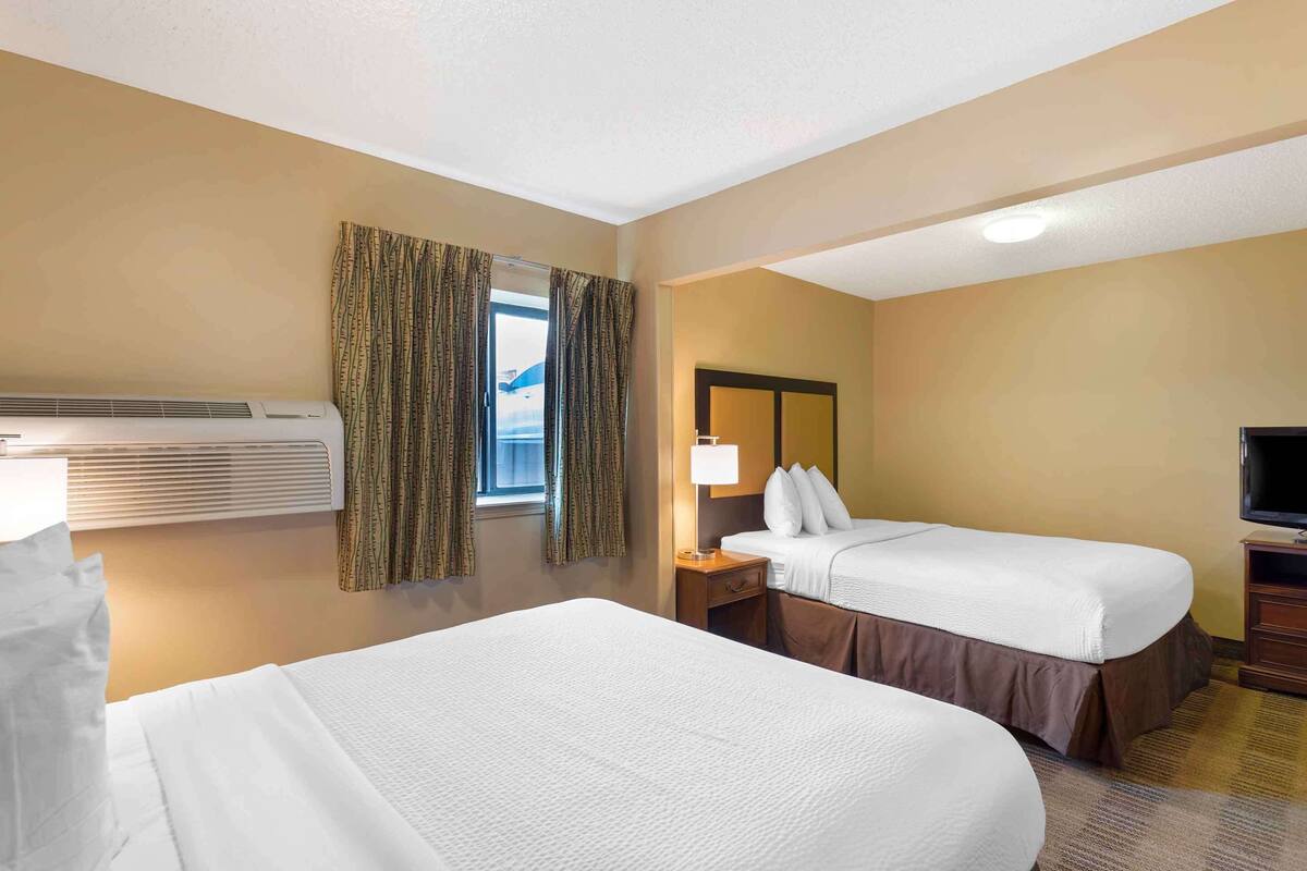 A hotel room with two beds, a TV, a lamp, and a window with curtains.