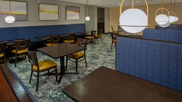 Un restaurant avec des banquettes et des tables, des sièges rembourrés en tissu bleu et des lampes suspendues.