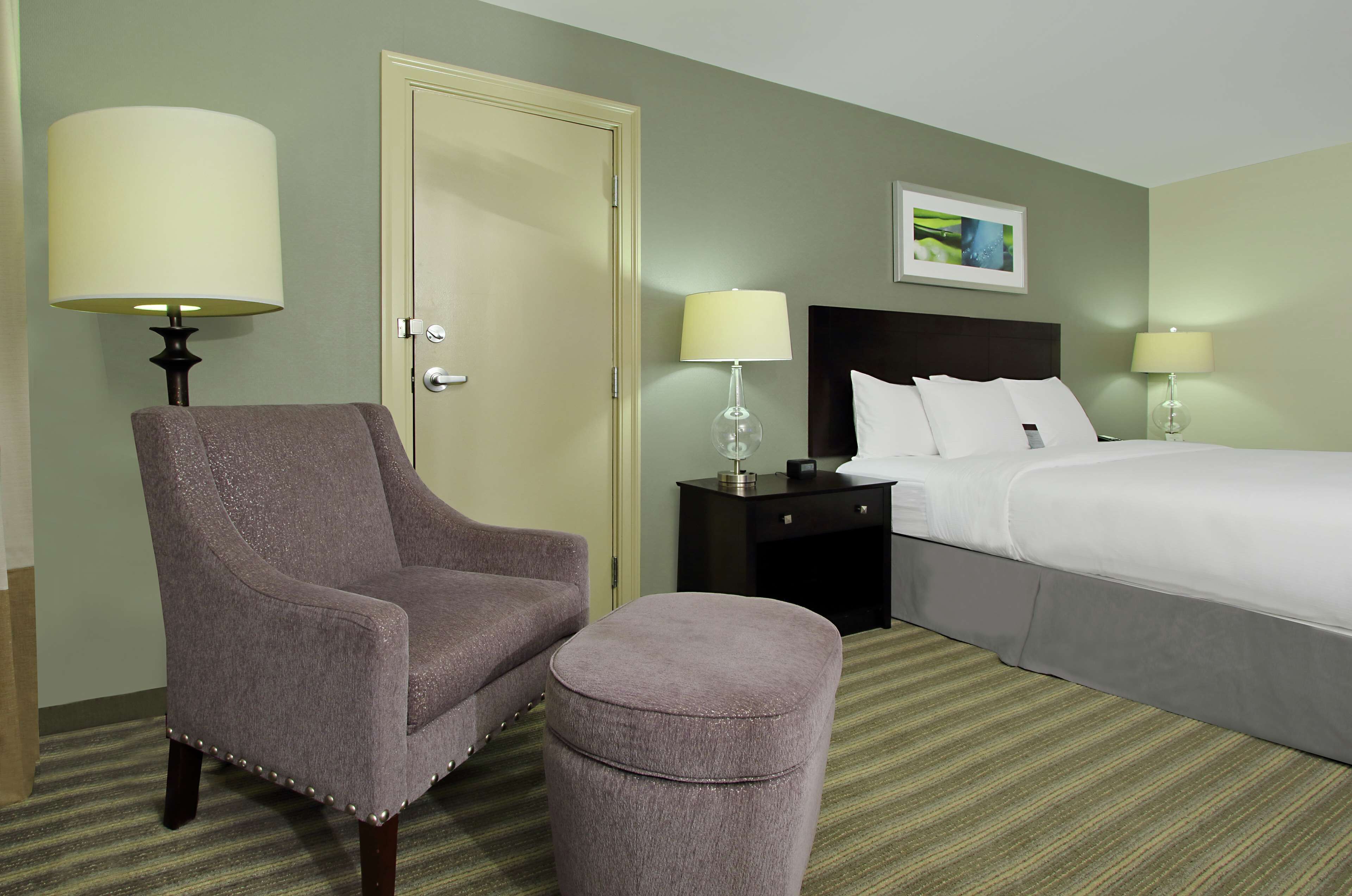 Una habitación de hotel con cama, una silla, una mesita de noche y una lámpara.