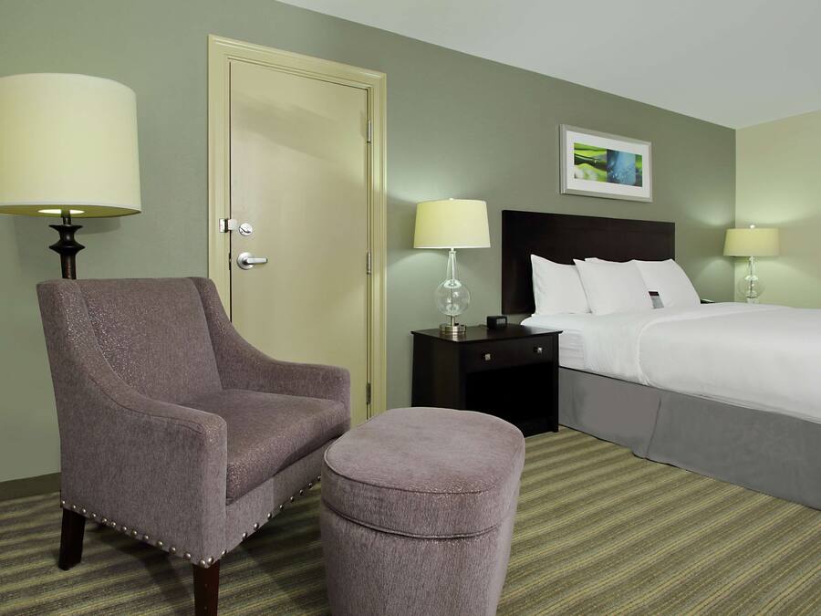 A hotel room with a bed, a chair, a nightstand, and a lamp.