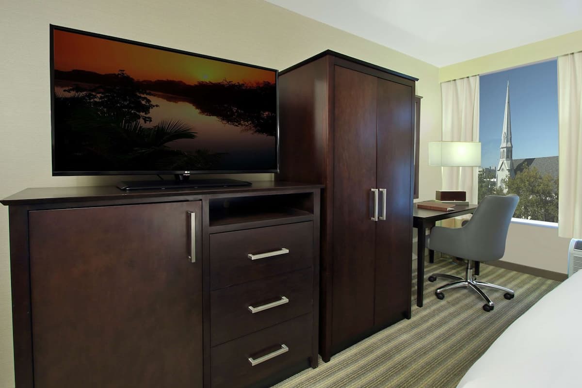 Una habitación de hotel con una televisión en un mueble, un escritorio con una silla y una ventana con vistas a la ciudad.