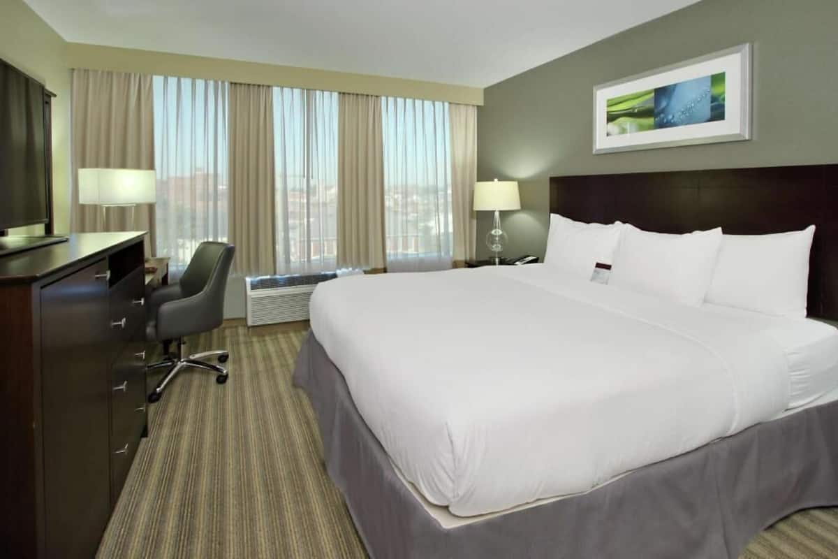 Una habitación de hotel con una cama grande, un escritorio con una silla, un televisor y una ventana con cortinas.