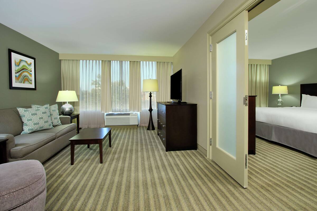 Habitación de hotel con sofá, una mesita, televisor, cama y escritorio con lámpara.