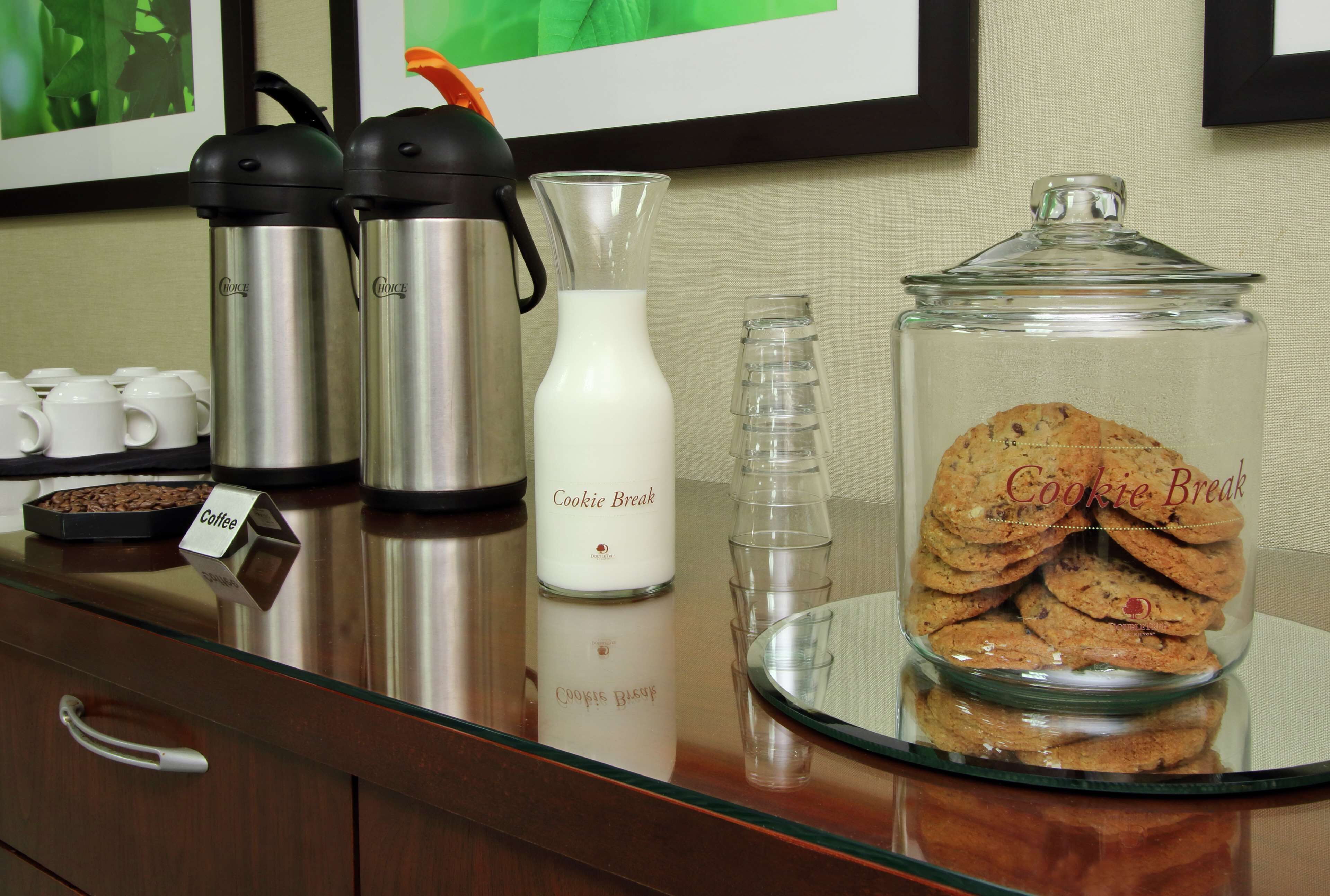 Una estación de café con dos máquinas de café, una jarra de leche y un tarro de galletas.