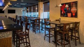 A restaurant with a long counter, multiple tables, and chairs. There are hanging lights and a large mural on the wall.