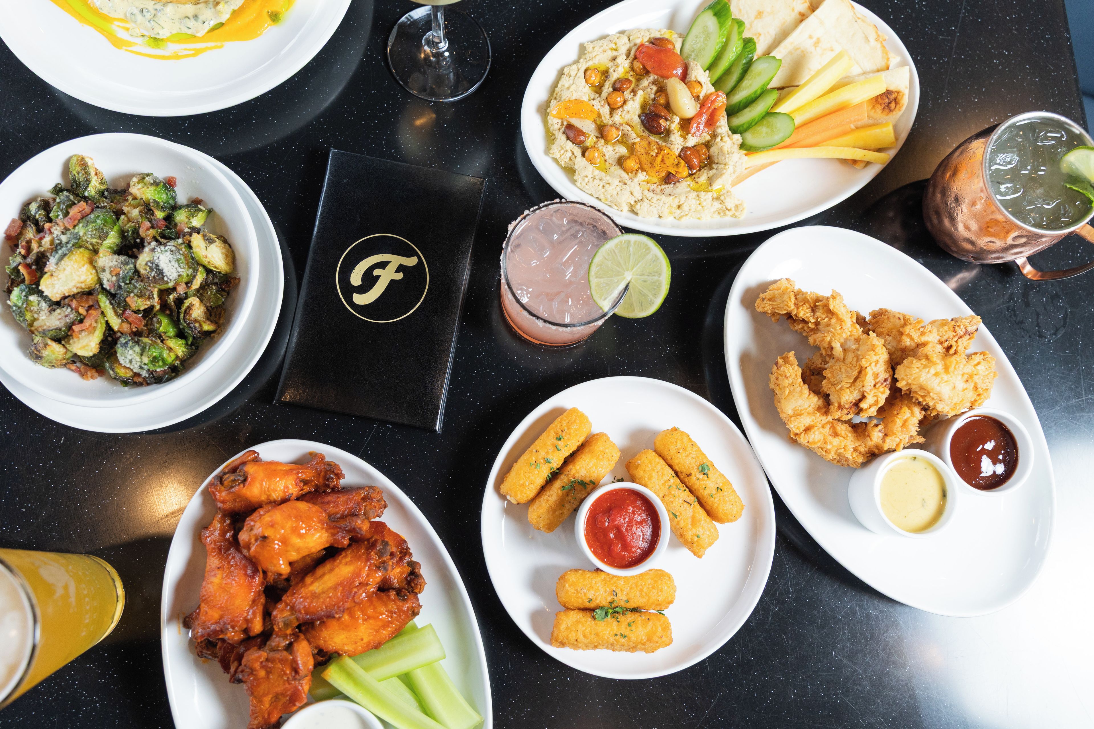 Une variété de plats, notamment des ailes de poulet, des frites et une salade, sont disposés sur une table.