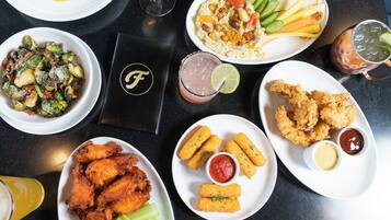 Une variété de plats, notamment des ailes de poulet, des frites et une salade, sont disposés sur une table.