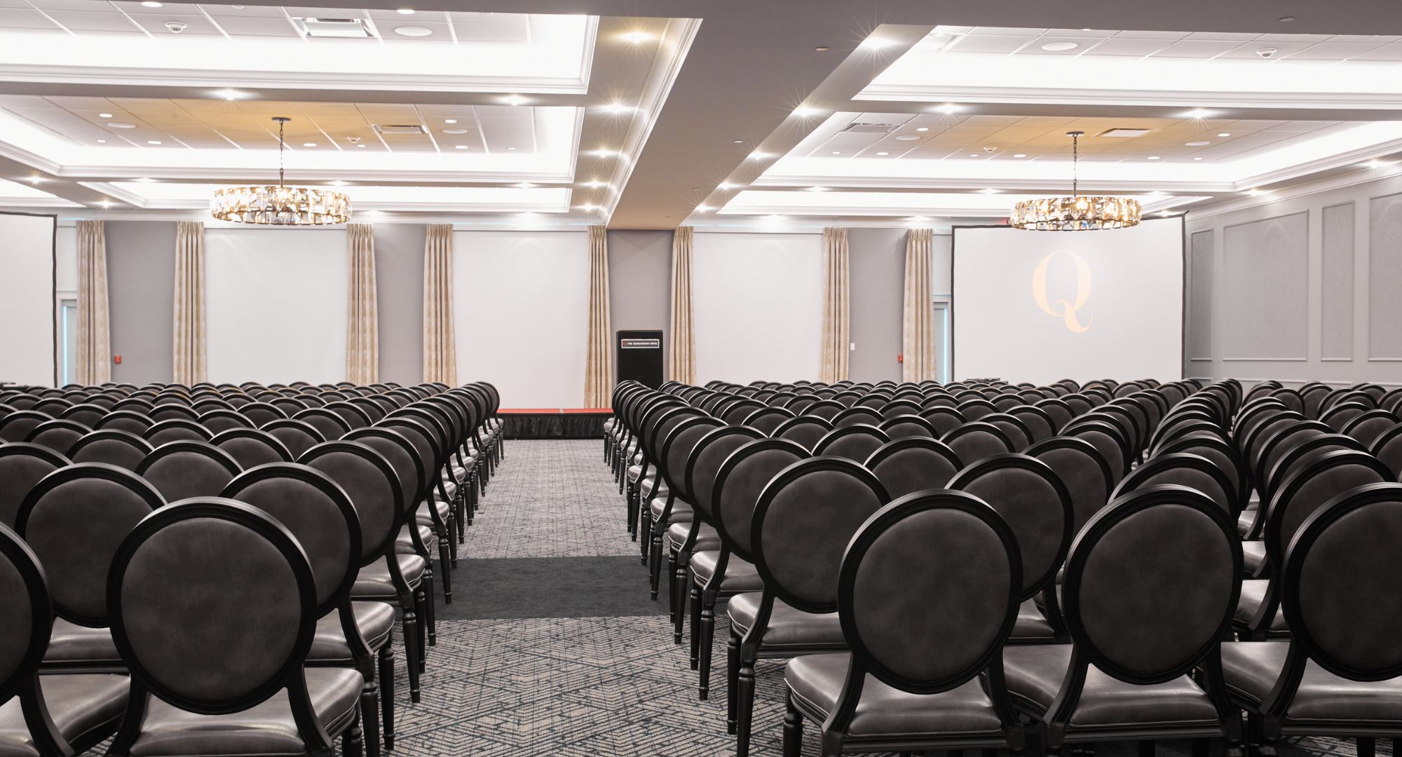 A conference room with rows of chairs, a podium, and a large screen.