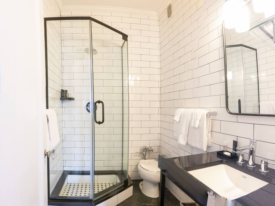 A modern bathroom with a glass-enclosed shower, white subway tiles, a black countertop sink, and a mirror above the sink.