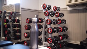 A gym with various weightlifting equipment, including dumbbells and a bench. - The Queensbury Hotel (Glens Falls)
