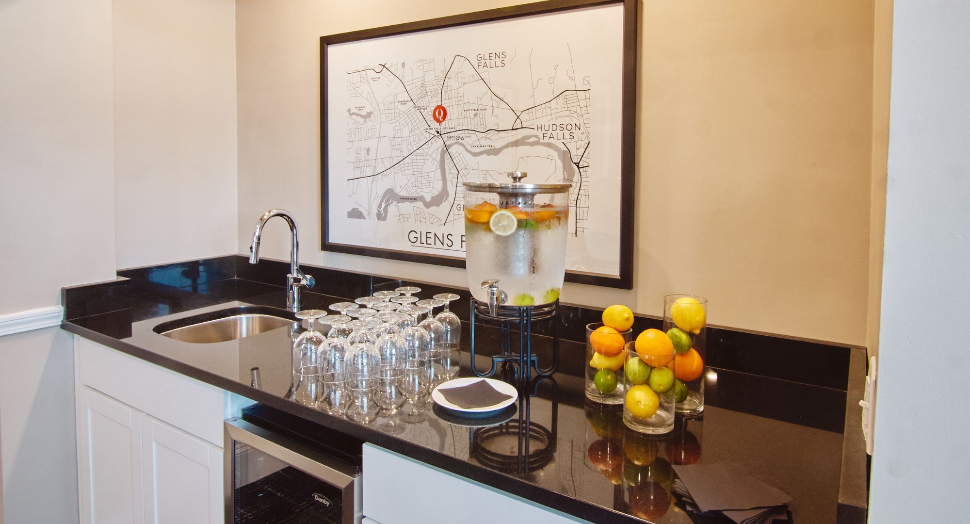 A kitchen with a sink, a map on the wall, a water dispenser, and glasses on the counter.