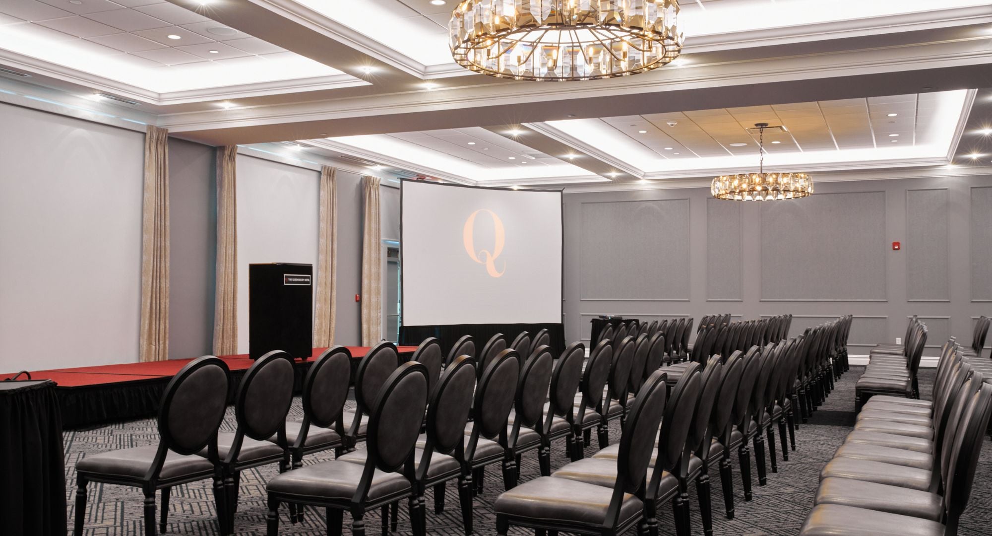 Ein Konferenzraum mit Stuhlreihen, einer Projektionsleinwand und einem Rednerpult.