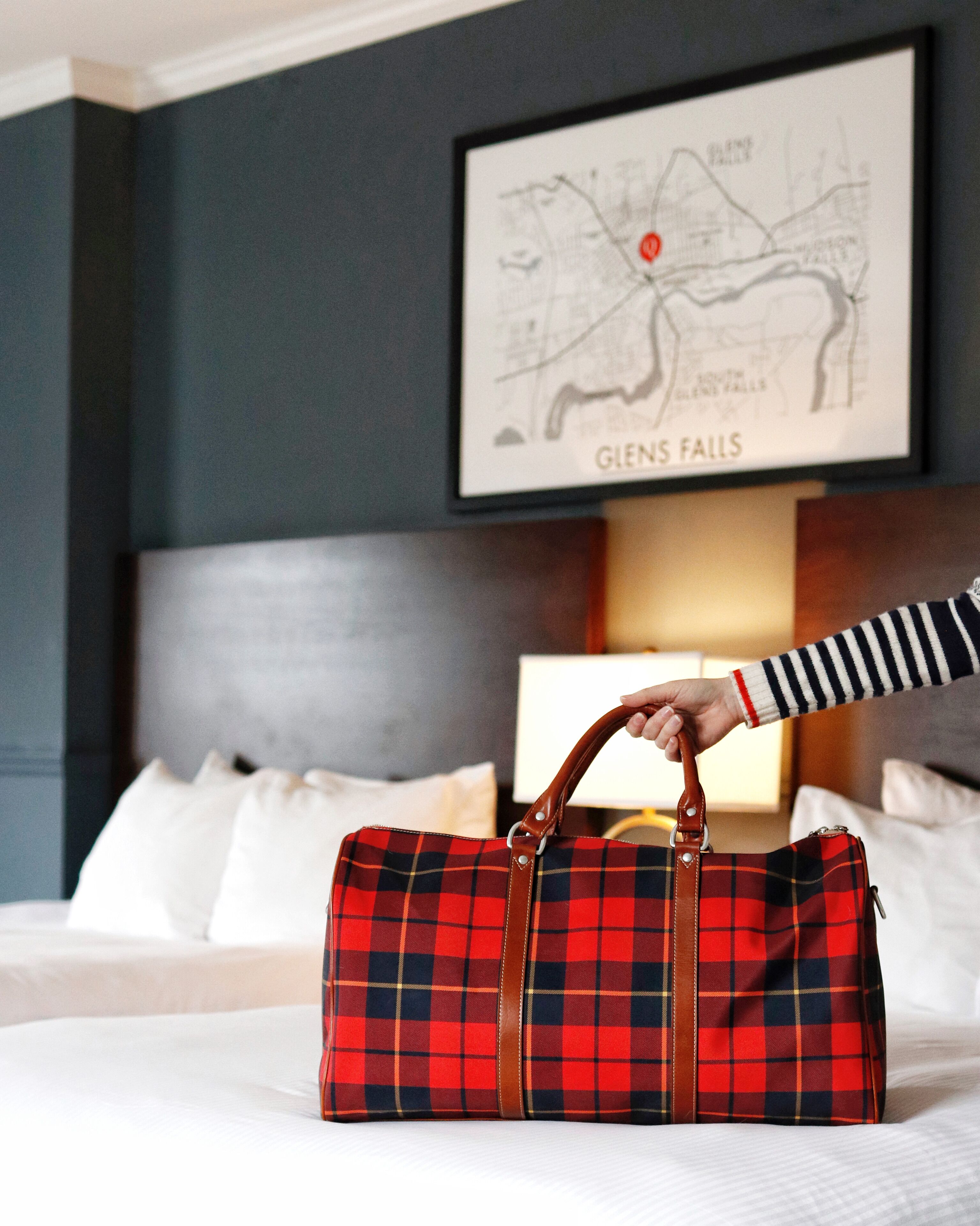 A hotel room with a bed, a map on the wall, and a plaid bag on the bed.
