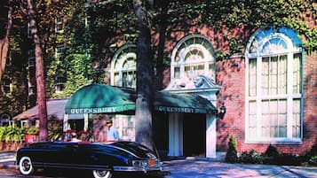 A vintage car parked in front of a building with 'Queensbury' signage.