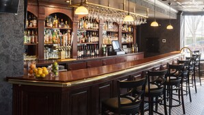 A bar area with a long counter, multiple shelves of bottles, and hanging wine glasses. - The Queensbury Hotel (Glens Falls)
