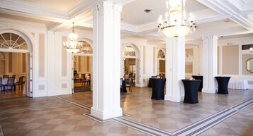A spacious hall with high ceilings, ornate columns, and chandeliers.