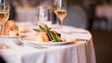 Uma mesa de jantar com um prato de comida, um garfo, uma faca e um copo de vinho branco.