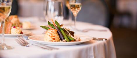A dining table with a plate of food, a fork, a knife, and a glass of white wine.