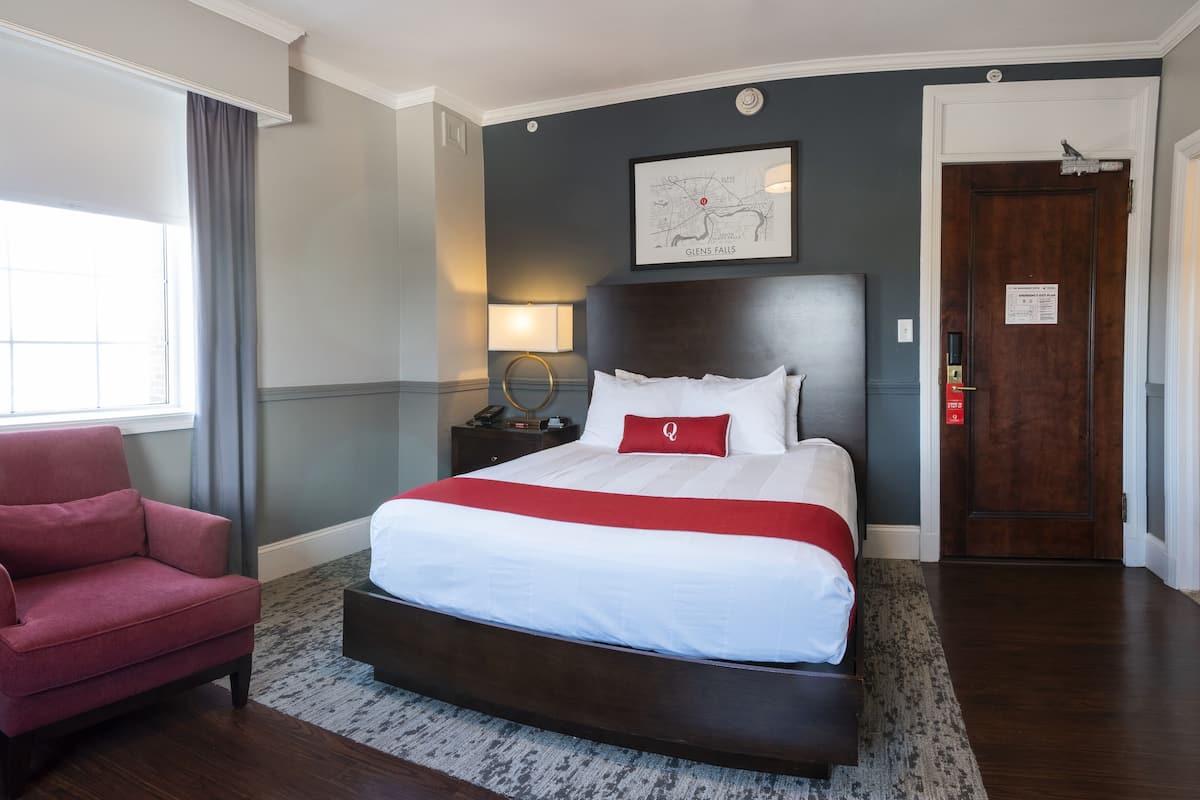 A hotel room with a large bed, a red armchair, a map on the wall, and a door with a sign.