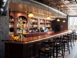A bar area with a long counter, multiple shelves of bottles, and a cash register.