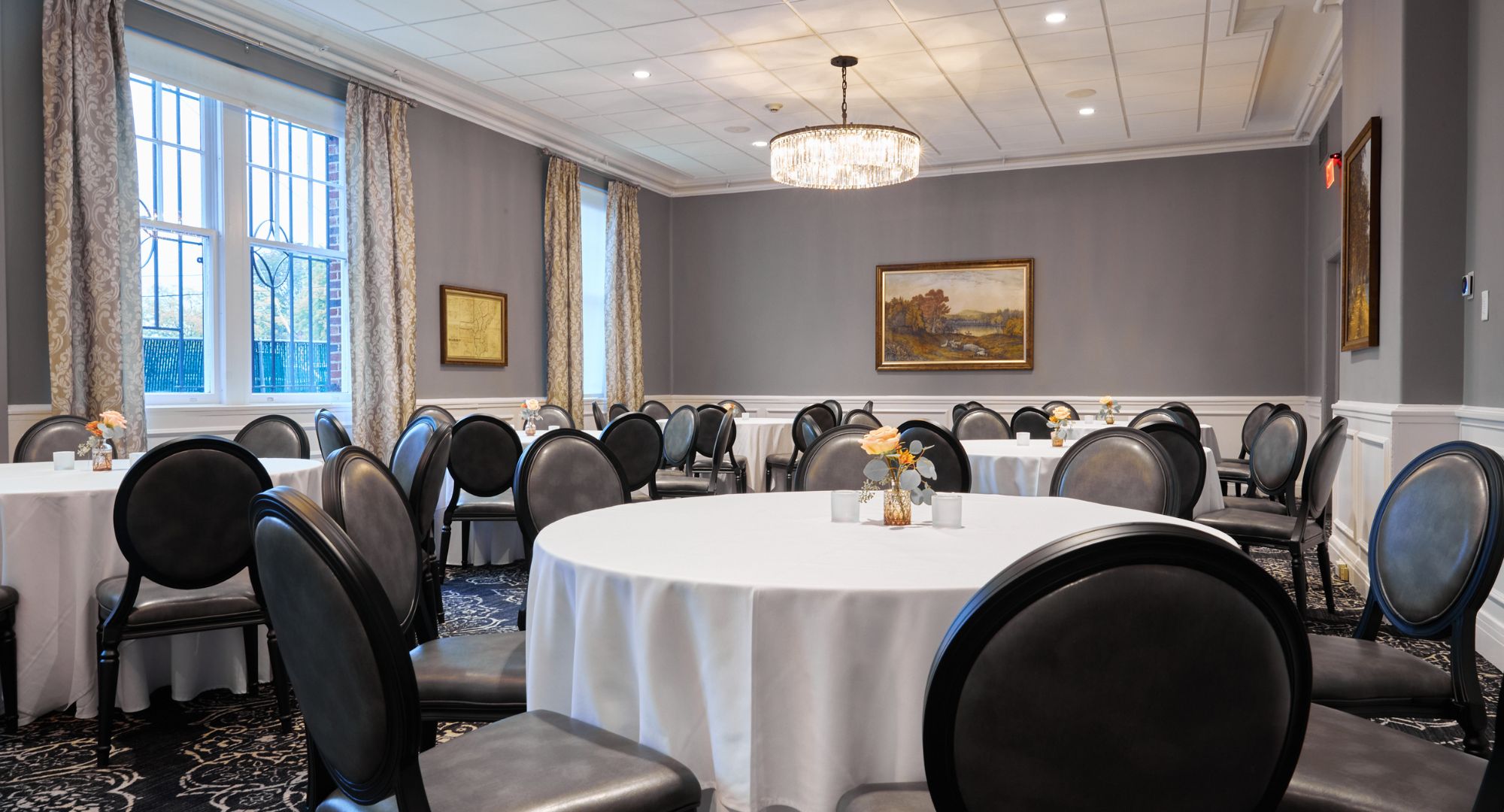 A conference room with round tables, black leather chairs, and a chandelier.